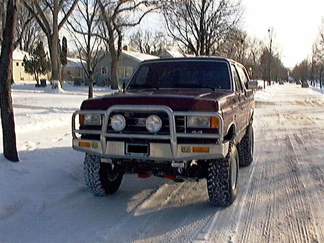 Maroon lifted Ford Bronco with chrome brush guard on snowy street, front view