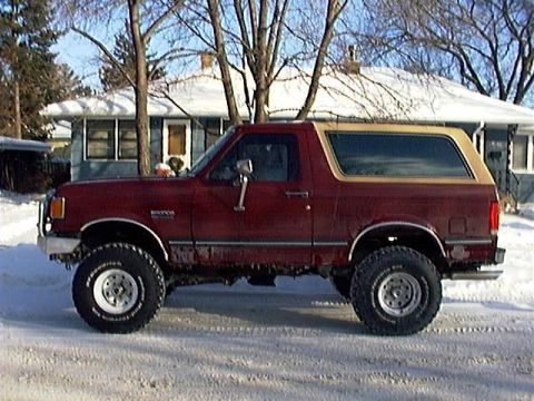 1991 Ford Bronco - Maroon 1991 Ford Bronco with a tan top sits on a snow-covered road in front of a house.