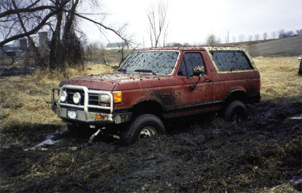 Red Ford Bronco stuck in deep mud in a rural field
