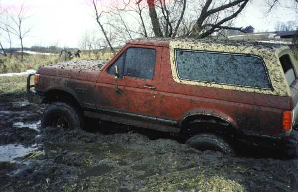 Red Ford Bronco SUV stuck deep in mud, side view, splattered with mud
