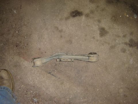 1992 Ford Bronco - A single automotive control arm with rubber bushings rests on a concrete surface.