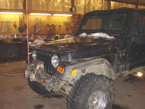 1992 Ford Bronco - A black Jeep Wrangler sits in a workshop, showing off its winch and off-road tires.