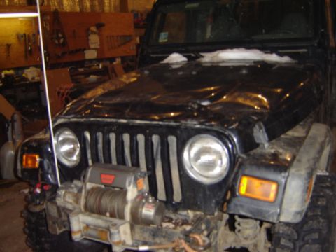 1992 Ford Bronco - Front view of a black Jeep Wrangler with a winch and snow on its hood, parked indoors.