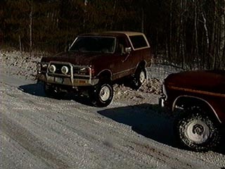 1991 Ford Bronco - A maroon 1980-1986 Ford Bronco is seen on a snowy road in a wooded area, with another vehicle partially visible on the right.