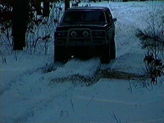 1991 Ford Bronco - A dark 1991 Ford Bronco navigates a snowy path, its brush guard equipped for the winter conditions.