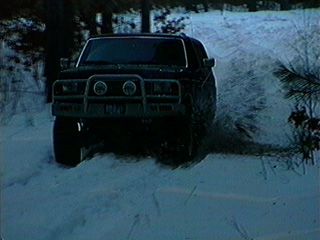 1991 Ford Bronco - A black 1992 Ford Bronco navigates a snowy path, its front grille and headlights visible.