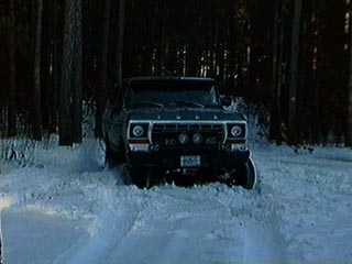 1991 Ford Bronco - A Ford Bronco navigates a snowy path through a wooded area, its front grille clearly visible.