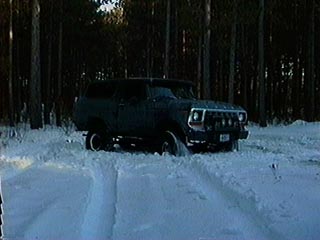 1991 Ford Bronco - A dark blue Ford Bronco is stuck in deep snow, surrounded by trees.