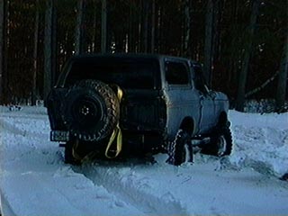 1991 Ford Bronco - A gray 1980-1986 Ford Bronco is seen from the rear, equipped with a spare tire, driving through a snowy landscape.