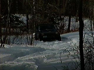 1991 Ford Bronco - A black Jeep Cherokee navigates a snowy path in a wooded area.