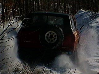 1991 Ford Bronco - This red SUV is driving through a snowy landscape, kicking up a lot of snow.