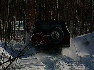 1991 Ford Bronco - A red SUV is stuck in a snowdrift, its rear end visible as it attempts to move forward.