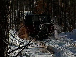 1991 Ford Bronco - A red SUV navigates a snow-covered path, kicking up snow as it moves forward.