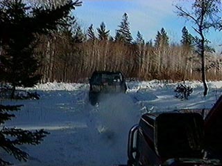 1991 Ford Bronco - A dark SUV drives through a snowy landscape, leaving a trail of disturbed snow behind it.