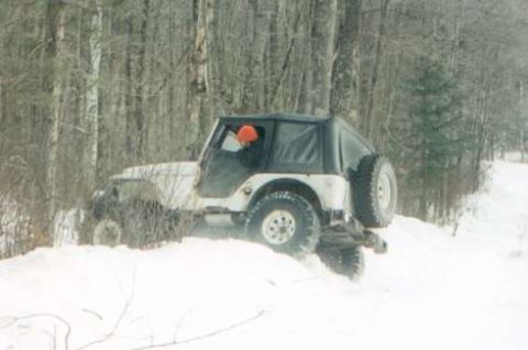 1991 Ford Bronco - A Jeep Wrangler navigates a snowy path surrounded by trees, with a driver visible inside.