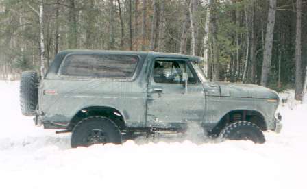 1991 Ford Bronco - A gray Ford Bronco navigates through a snowy forest, kicking up snow as it moves.