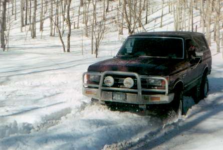 1991 Ford Bronco - A dark red 1992 Ford Bronco navigates a snowy forest road, kicking up snow.