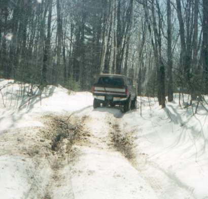 1991 Ford Bronco - This Ford Bronco, likely from the 1987-1991 model years, navigates a challenging snowy and muddy path in a wooded area.