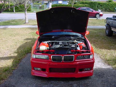 1995 BMW M3 - The front of a red 1995 BMW M3 is visible with its hood open, revealing the engine compartment.