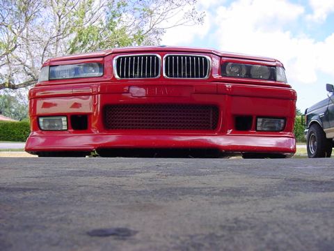 1995 BMW M3 - The front of a red BMW sedan is shown, with a portion of a green pickup truck visible to the right.