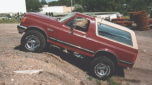 1991 Ford Bronco - A red 1991 Ford Bronco with a tan top is shown on a dirt incline, equipped with aftermarket wheels and side steps.