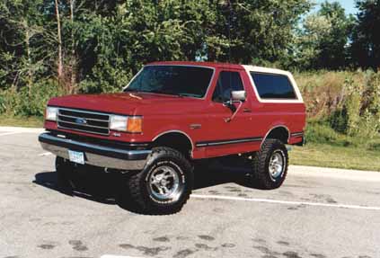 1991 Ford Bronco - This red Ford Bronco with a white top is shown from the front-left angle.