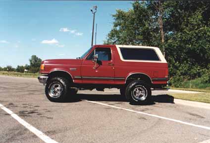 1991 Ford Bronco - This red 1991 Ford Bronco features a white removable top and is parked on asphalt.