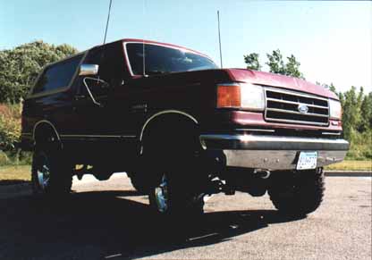 1991 Ford Bronco - This maroon Ford Bronco is shown from a 3/4 front angle, revealing its chrome bumper and aftermarket wheels.