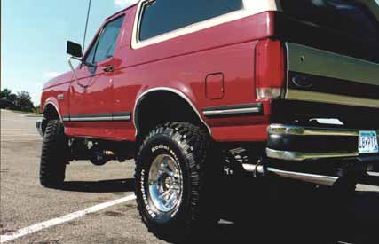 1991 Ford Bronco - This red 1991 Ford Bronco features a lifted suspension and chrome wheels, seen here in a rear three-quarter view.
