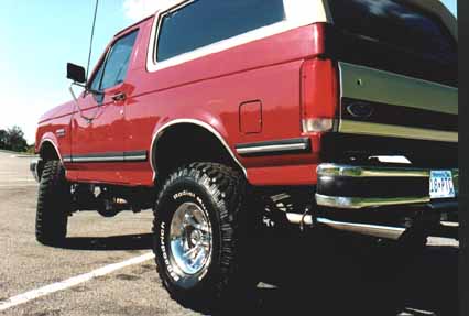 1991 Ford Bronco - This red Ford Bronco features a lifted suspension and large off-road tires, suggesting a model year later than claimed.