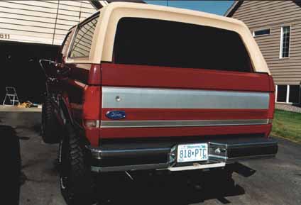 1991 Ford Bronco - The rear of a red Ford Bronco with a tan removable top is parked in a driveway.