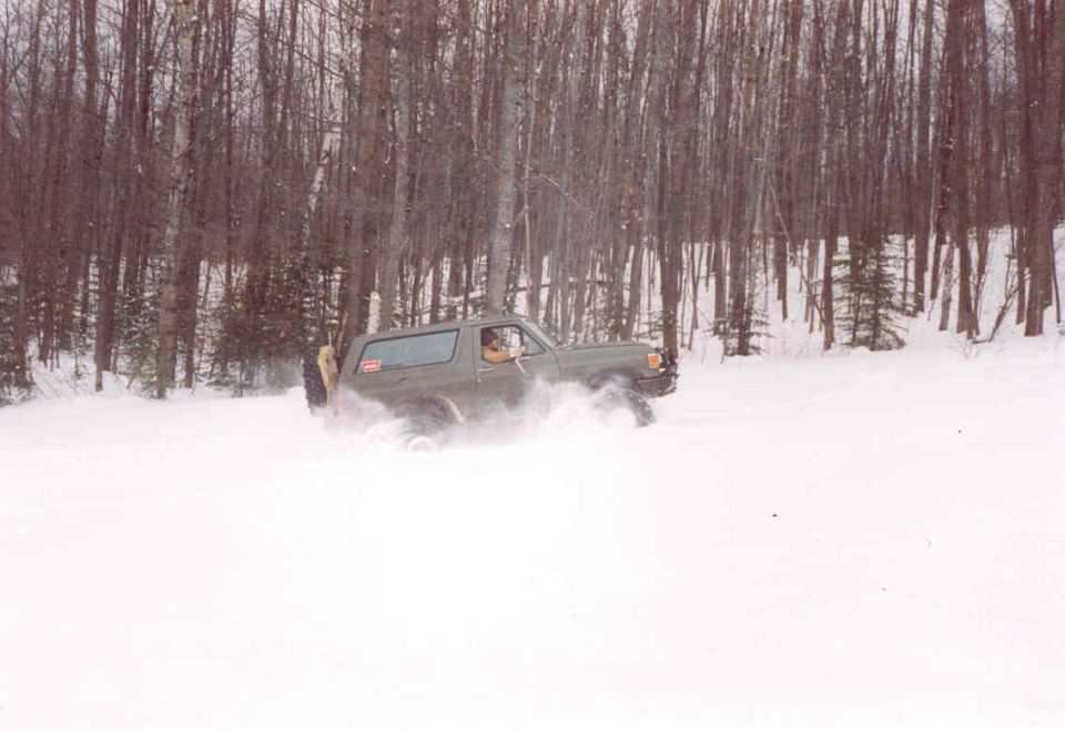 Green Ford Bronco driving through snow, spare tire on rear door