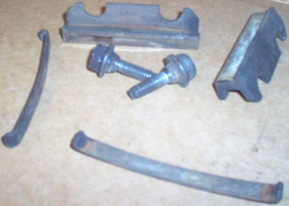 Two metal U-shaped brackets, two flange bolts and two curved tabs laid out on cardboard