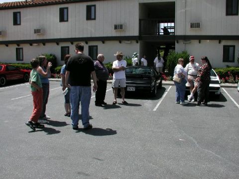 1986 Pontiac Fiero - A group of people gather around a black 1986 Pontiac Fiero in a parking lot.