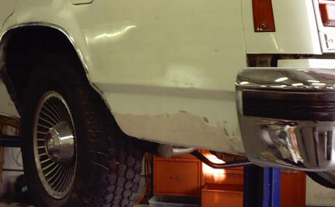 1985 Ford LTD Crown Victoria - Rear quarter panel of a white 1985 Ford Crown Victoria LTD shows signs of rust and damage near the wheel well and bumper.
