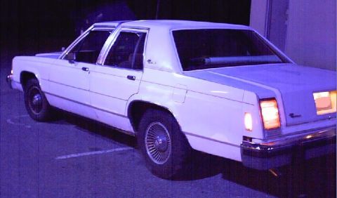 1985 Ford LTD Crown Victoria - This white sedan is parked in a lot, with its rear lights on.