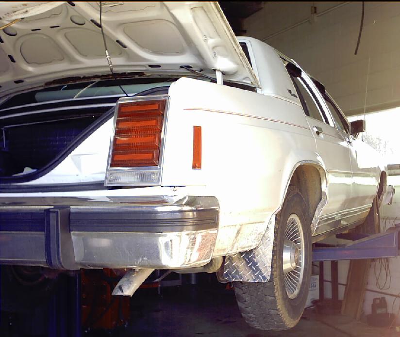 White sedan on a lift, rear view. Open trunk, chrome bumper, diamond plate mud flap