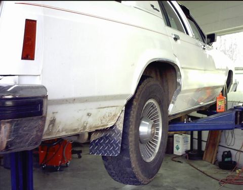 1985 Ford Crown Victoria LTD - A white 1985 Ford Crown Victoria LTD is shown on a car lift, revealing its side profile and rear wheel.
