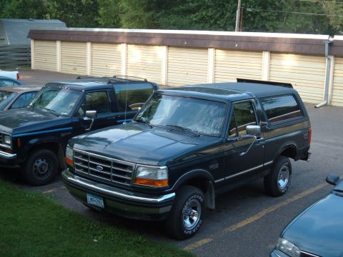 1994 Ford Bronco - 1994 Ford Bronco parked in front of storage units with another vehicle beside it.