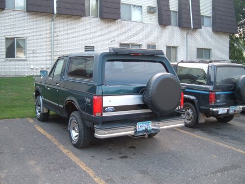 1994 Ford Bronco - Two Ford Broncos are parked in a lot outside an apartment building.