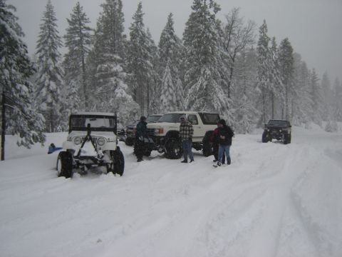 1991 Ford Bronco - Several off-road vehicles are parked in a snowy forest scene with people gathered around.