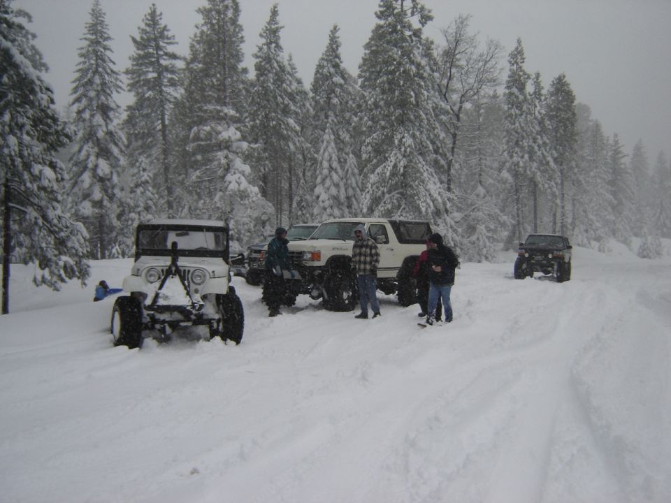 White lifted Ford Bronco and plow-equipped Jeep parked in deep snow with people