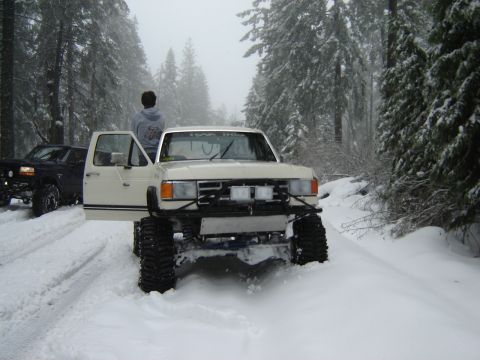 1991 Ford Bronco - Modified 1987 Ford Ranger with large tires navigates a snowy forest road, with another truck visible behind it.