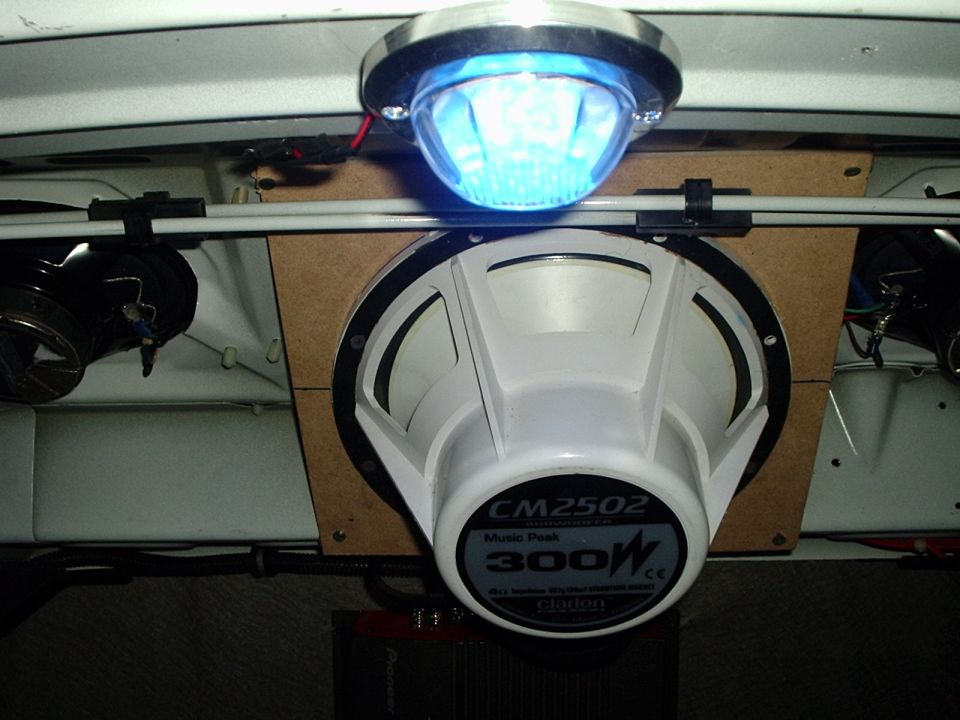 Car interior with a large subwoofer, blue dome light, and amplifier. Text on subwoofer reads CM2502 300W