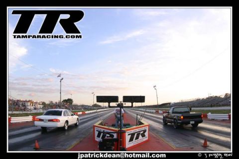1997 Ford Crown Victoria - Two vehicles compete on a drag strip under a cloudy sky.