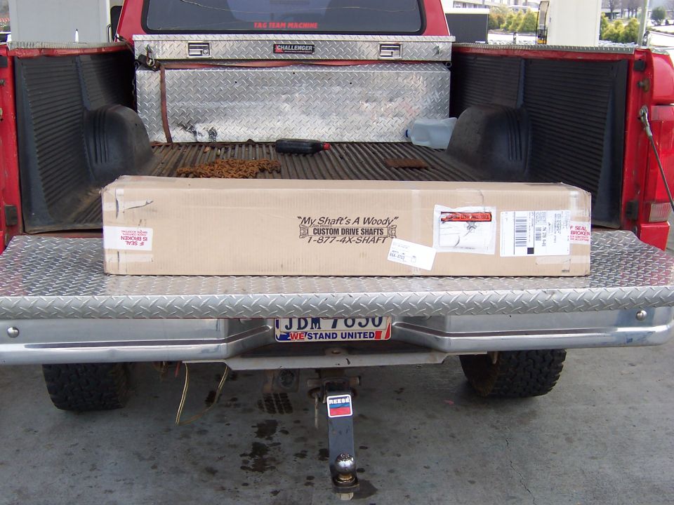 Open tailgate of a red lifted pickup with a long Custom Drive Shafts box, diamond-plate bumper, US plate JDM 7050