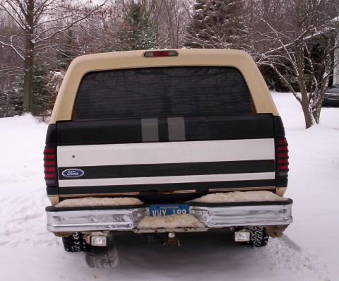 1993 Ford Bronco - Rear view of a tan and black Ford Bronco parked in the snow, showing its chrome bumper and license plate.