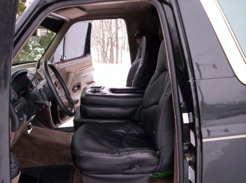 1993 Ford Bronco - The interior of the vehicle shows plush leather seats and a large center console with cup holders.