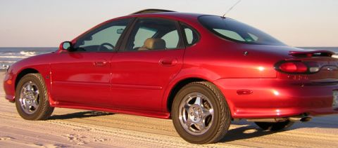 1997 Ford Taurus - A red sedan is parked on the beach with the ocean in the background.