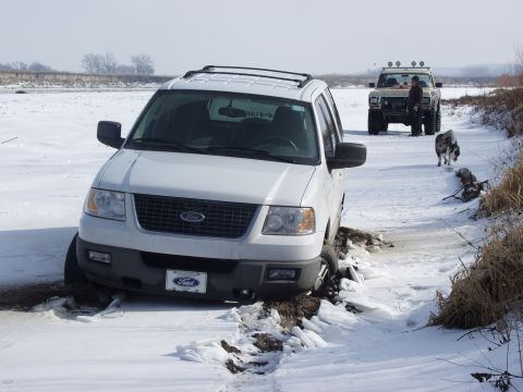 1979 Ford Bronco - Two SUVs are stuck in a snowy, muddy path, with one vehicle deeply mired in the foreground.